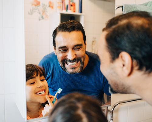 Father and young daughter brushing their teeth together