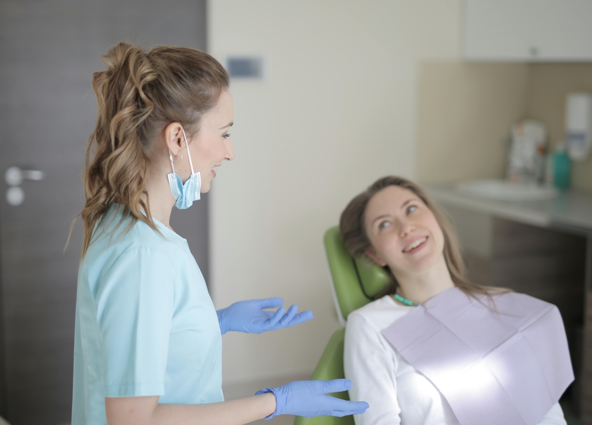 A woman sits in a dental chair while a dentist speaks to the patient about her dental care.