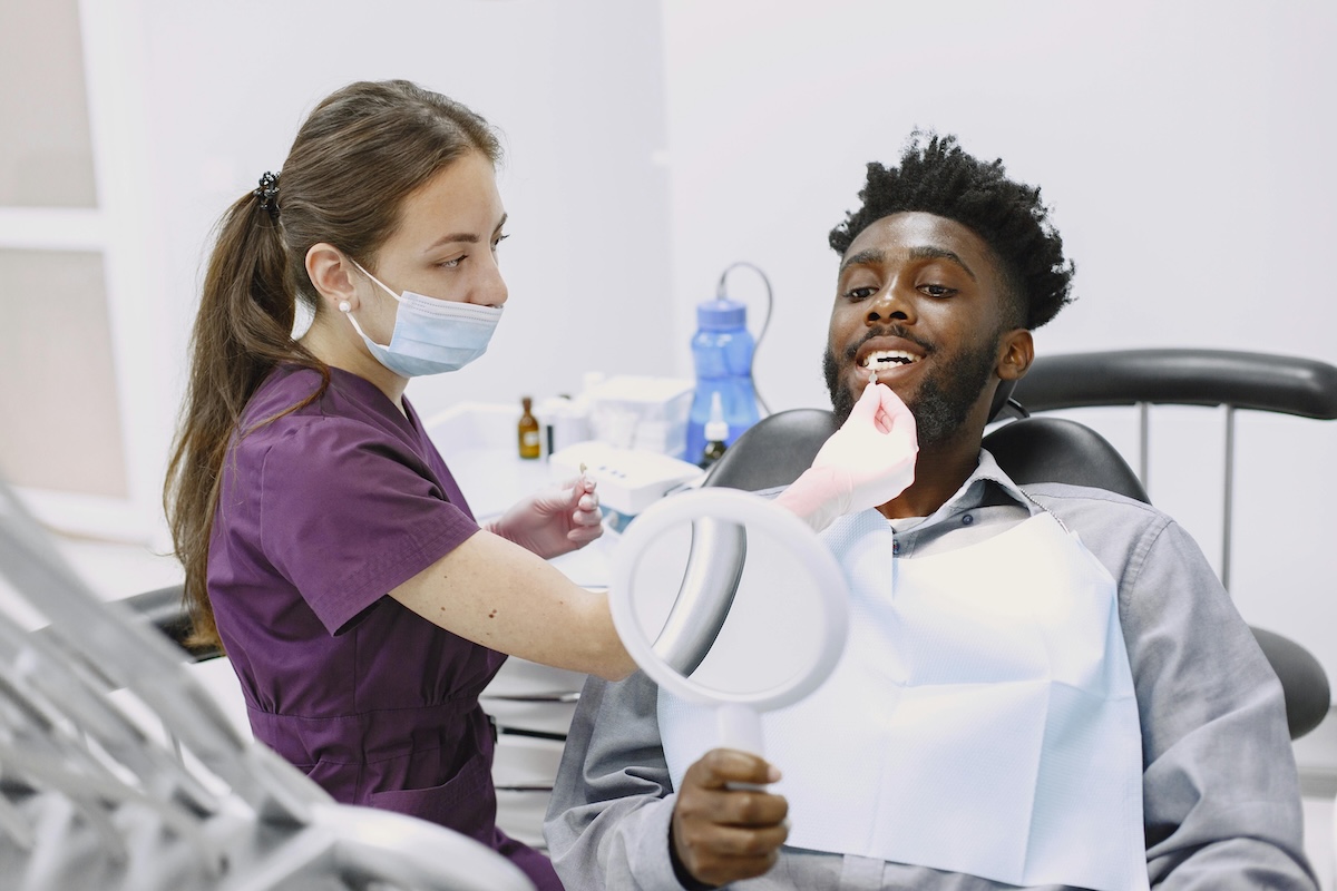 A man reclines in a dental chair while a dentist cleans his teeth, focusing on dental implants.