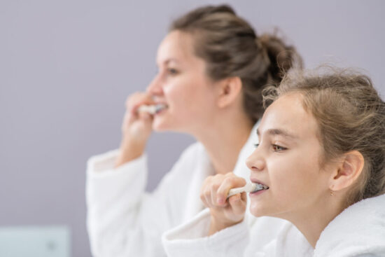 Mom and daughter brush their teeth in front of the bathroom mirror.