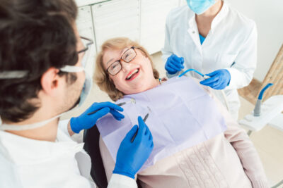 A woman sits in a dental chair with a dentist and a nurse, engaged in a dentistry-related consultation