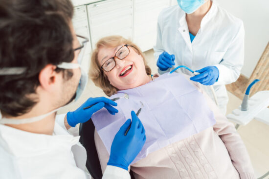 A woman sits in a dental chair with a dentist and a nurse, engaged in a dentistry-related consultation