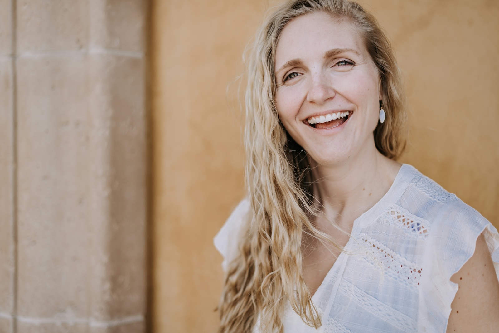 A smiling woman with long blonde hair, showcasing her healthy teeth in a dental office setting.