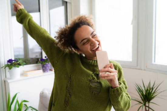 A woman joyfully holds her phone, displaying her dental teeth whitening, with a focus on her radiant smile.