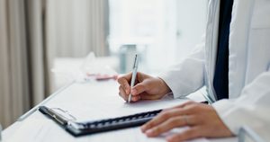 Hands of medical professional writing in patient's chart
