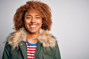 Young beautiful African American afro woman with curly hair wearing casual winter coat with a happy face standing and smiling with a confident smile showing teeth.