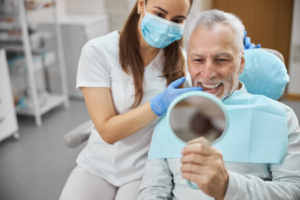 a man looking at his teeth in a dental office using a handheld mirror